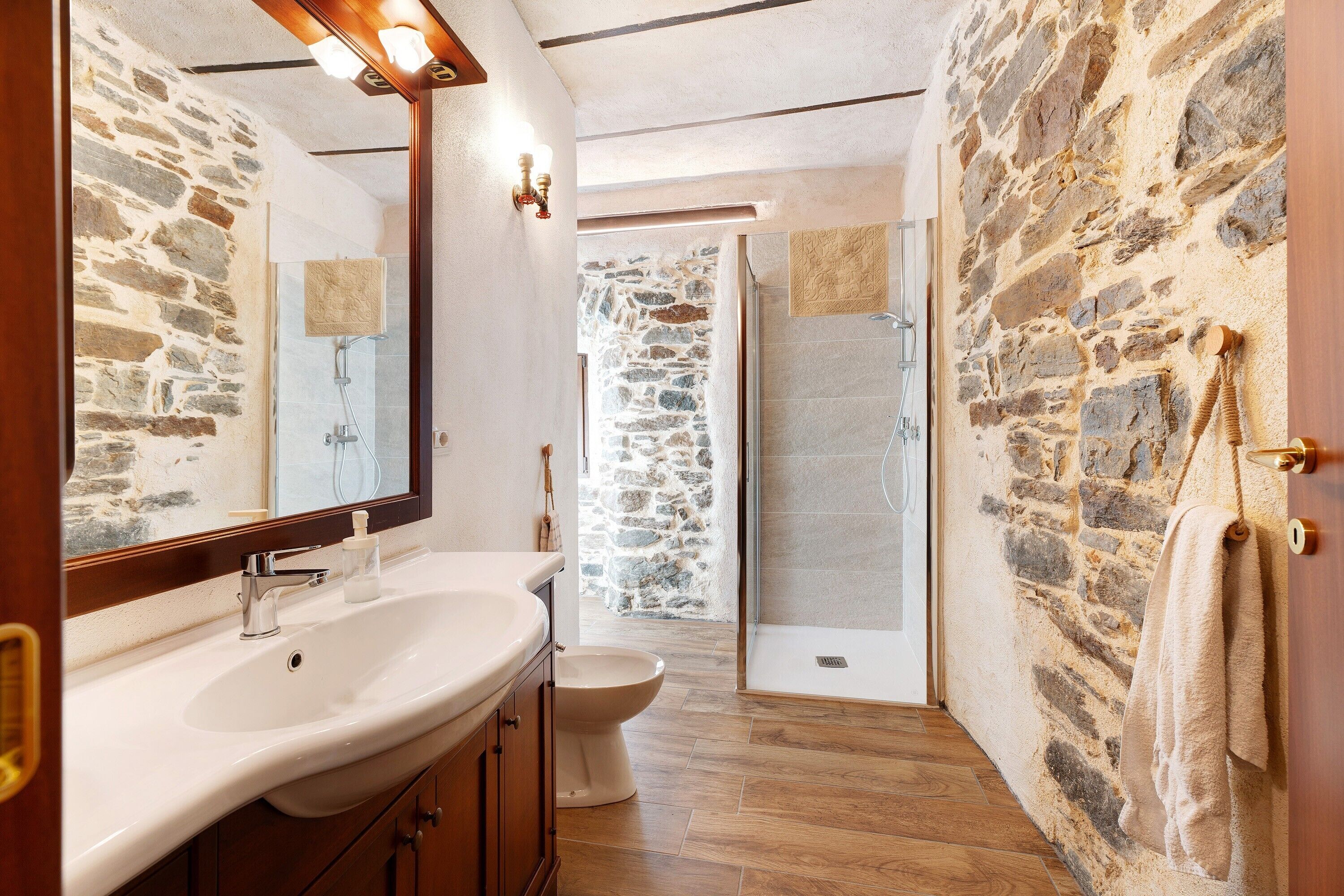 A bathroom with a stone wall, a sink, a toilet, and a shower area.