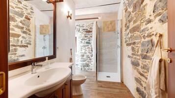 A bathroom with a stone wall, a sink, a toilet, and a shower area.