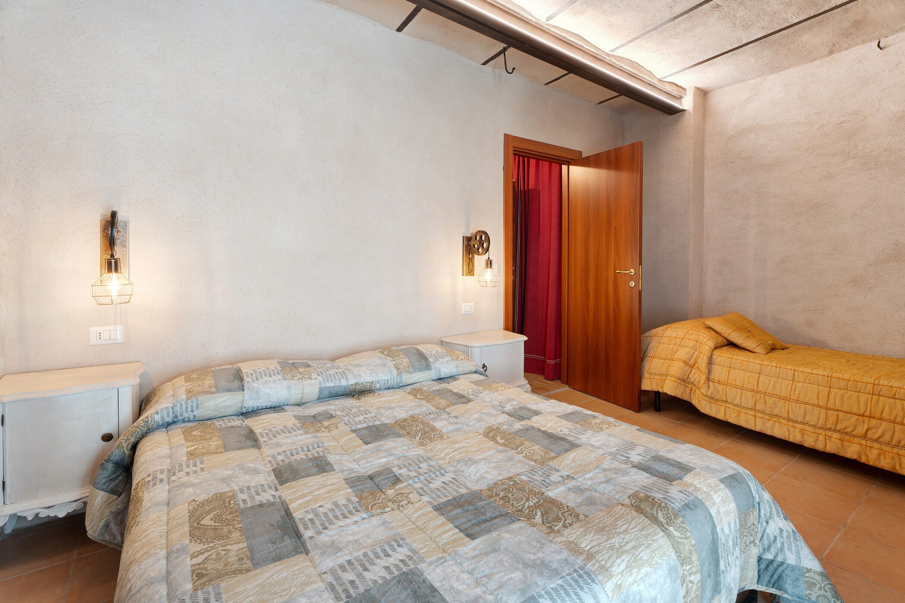 A bedroom with a large bed, a smaller bed, a nightstand, a wardrobe, and a red curtain.