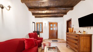 A living room with a red sofa, wooden ceiling beams, a TV, and a wooden cabinet. - Holiday Home 'Casa Vacanze Laghi e Monti' with Mountain View, Private Garden and Wi-Fi (Mergozzo)