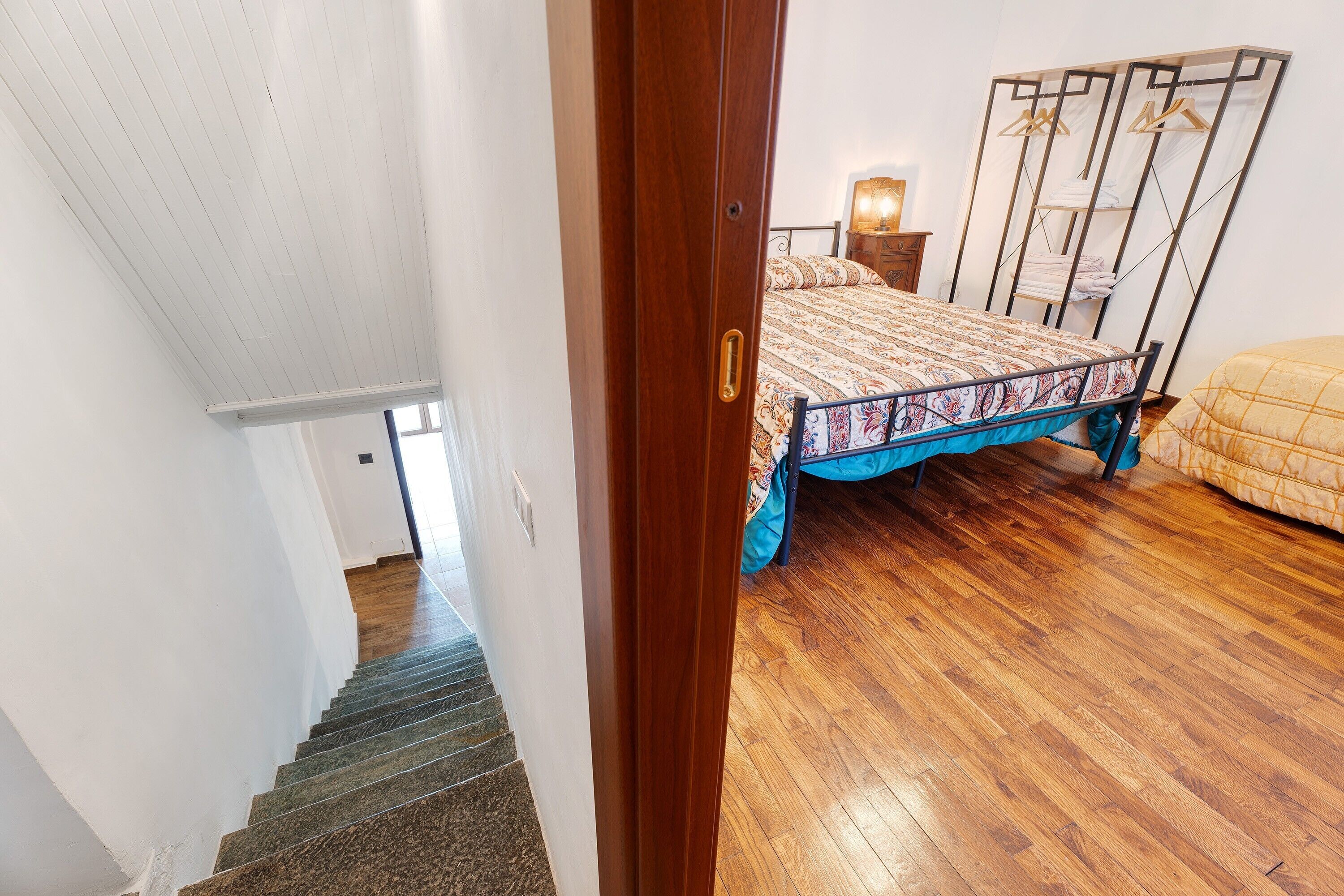 A bedroom with a bed, a wardrobe, a nightstand, and a staircase.