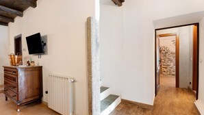 A room with a wooden dresser, a television mounted on the wall, a stone pillar, and a staircase leading to another room. - Holiday Home 'Casa Vacanze Laghi e Monti' with Mountain View, Private Garden and Wi-Fi (Mergozzo)