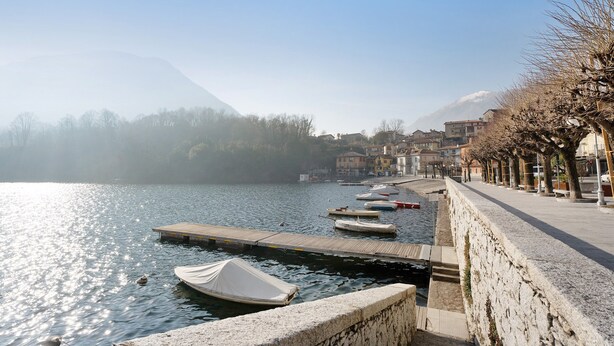 A lakeside view with boats docked, a stone wall, and buildings in the background. - Holiday Home 'Casa Vacanze Laghi e Monti' with Mountain View, Private Garden and Wi-Fi (Mergozzo)