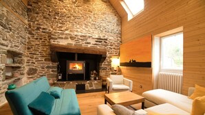 A cozy room with a stone wall, a fireplace, and a large window. - Gite Finistère for 7: Private Pool & Spa, Garden, 4 km from Beaches (PEUMERIT)
