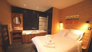 A bedroom with a wooden floor, a bed with white linens, a wooden headboard, a bedside table, a mirror, and a wall-mounted artwork. - Gite Finistère for 7: Private Pool & Spa, Garden, 4 km from Beaches (PEUMERIT)