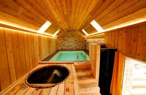 Una sauna de madera con pared de piedra, bañera de hidromasaje y zona de ducha.