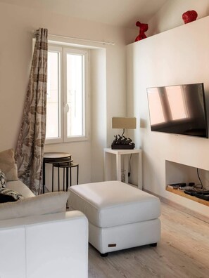 Ein modernes Wohnzimmer mit einer Couch, einem kleinen Tisch, einer Lampe und einem an der Wand befestigten Fernseher.