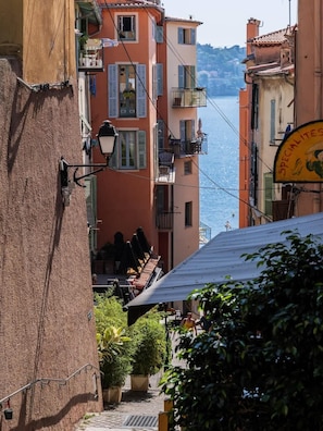 Un vicolo stretto con edifici, un cartello con la scritta 'Specialites' e vista sul mare.