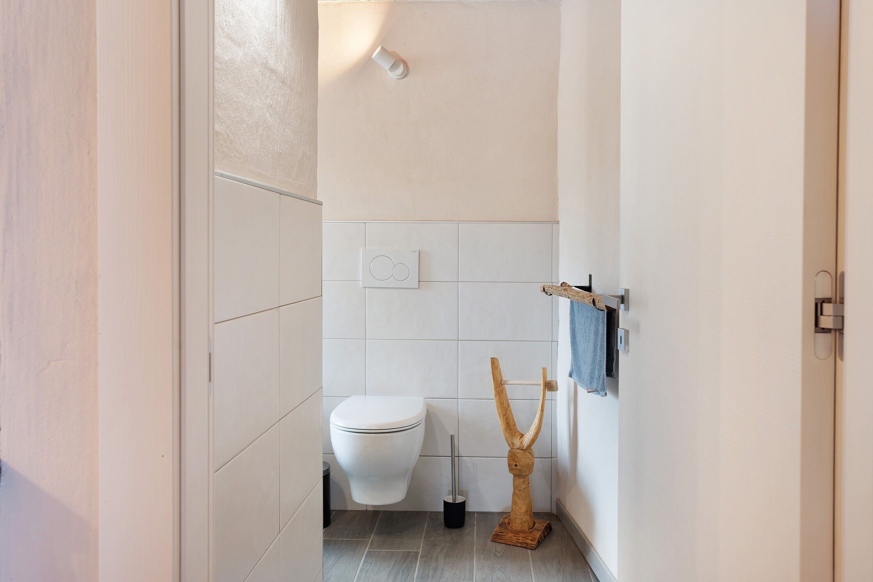 A bathroom with a toilet, a hand dryer, and a wooden towel rack.