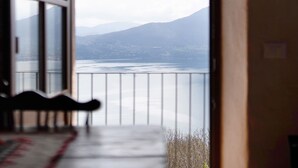 Uitzicht door een raam met een bank en een leuning, op een waterpartij en verre bergen.