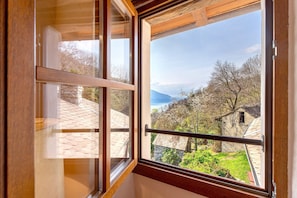 A window with a view of a stone building, a metal railing, and a clear sky.