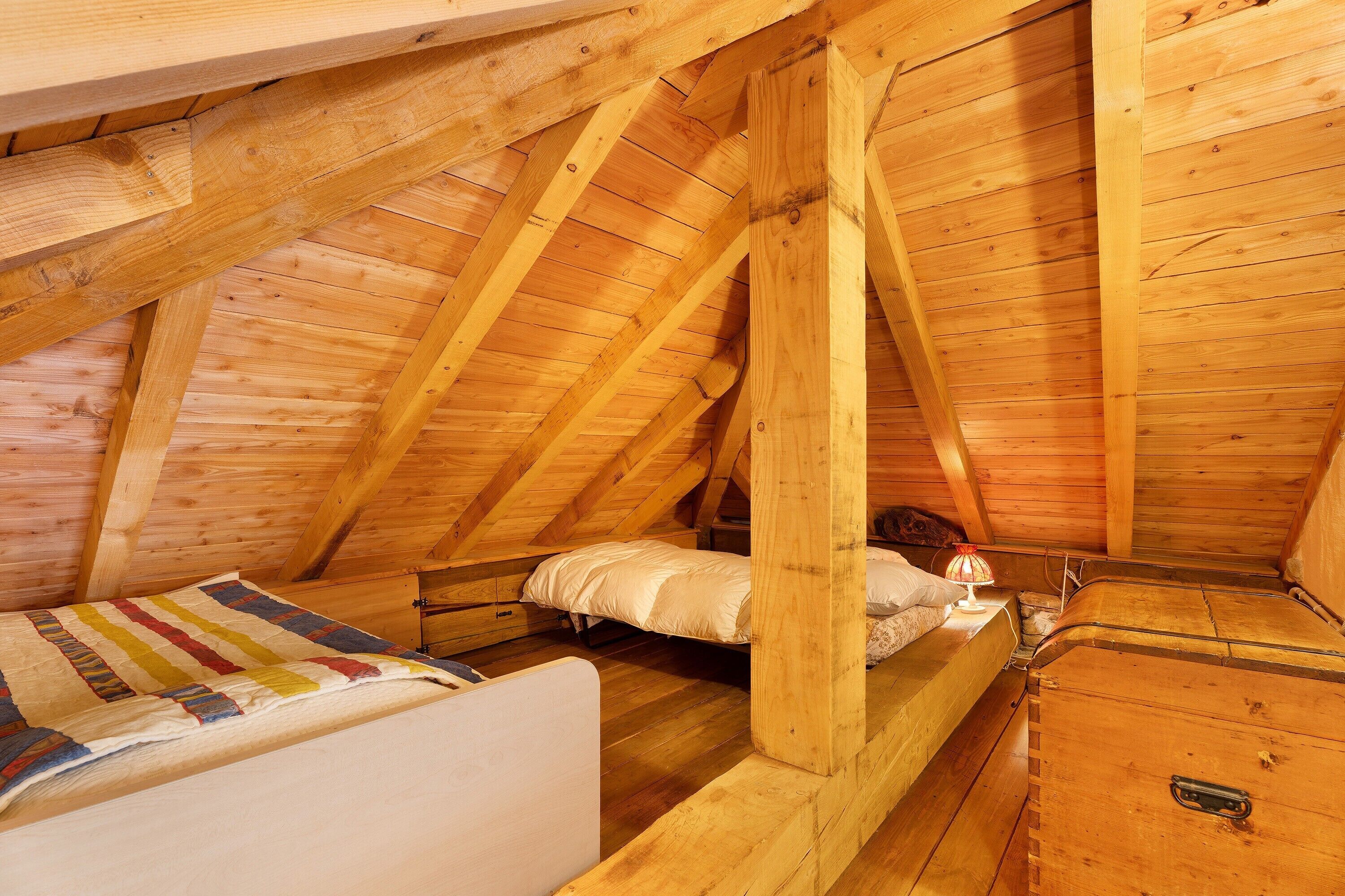 A small, cozy attic bedroom with wooden beams, a single bed, a dresser, and a nightstand.