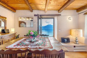 Ein Holzespeisesaal mit Tischdecke, Stühlen, einer Lampe, einem Lautsprecher und Meerblick durch ein Fenster.