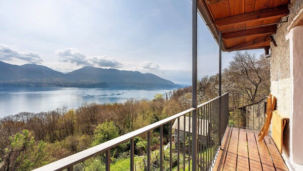 Een balkon met een houten vloer, een metalen hekwerk en uitzicht op een meer en bergen.