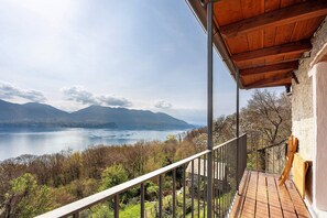 Een balkon met een houten vloer, een metalen hekwerk en uitzicht op een meer en bergen.