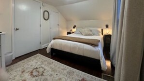 Un dormitorio con cama, mesitas de noche, una alfombra e iluminación en el techo.