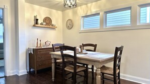 Un comedor con una mesa de madera, cuatro sillas, un reloj y una estantería decorada.