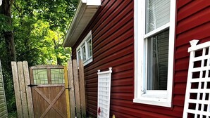 Un sendero en un jardín que lleva a una casa roja con una verja de madera y una cerca blanca.