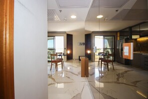 A modern hotel lobby with marble flooring, wooden chairs, and a reception desk. - OZPED Flats Particulares Brasil 21  (Brasília)