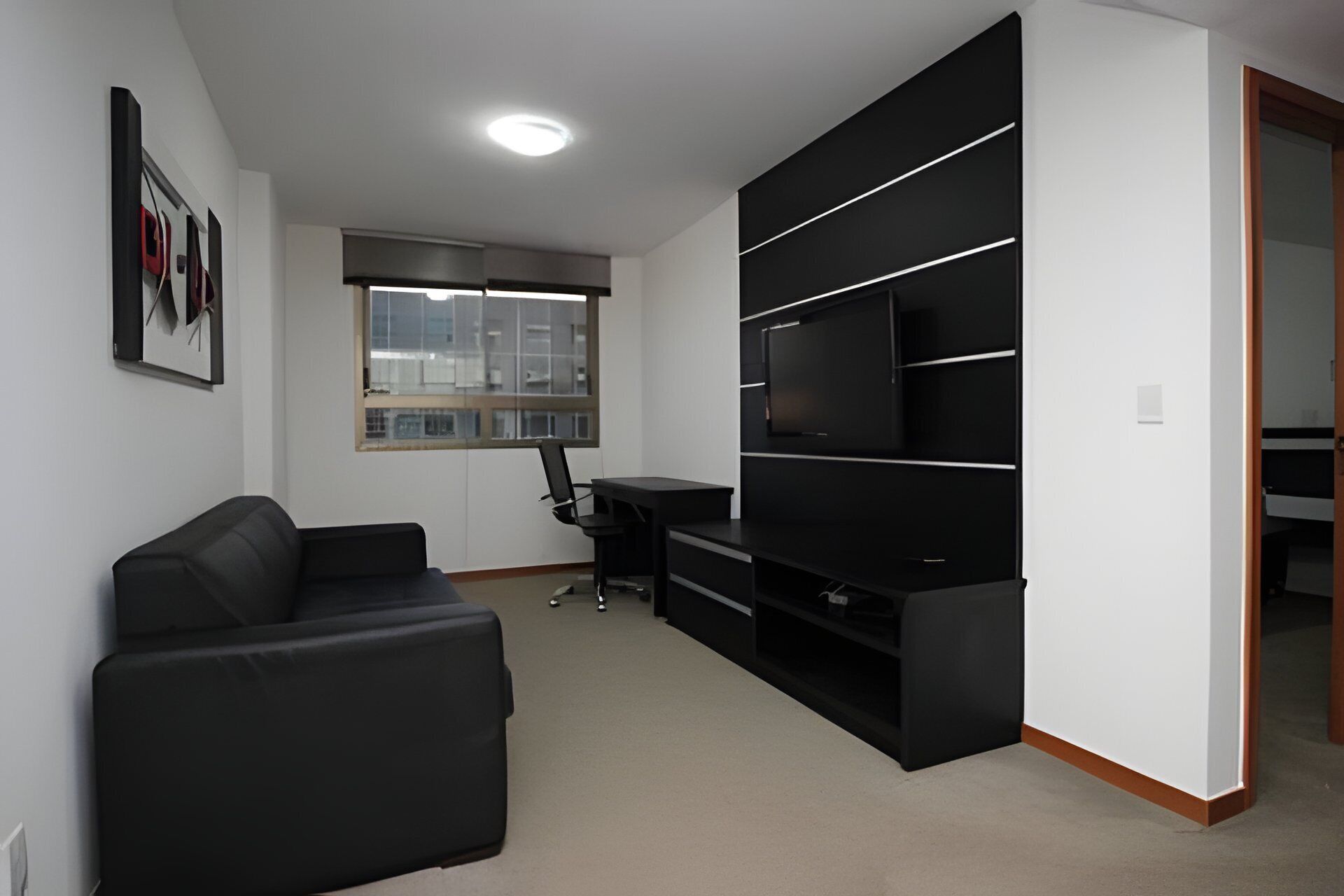 Un salon moderne avec un canapé noir, un bureau et un téléviseur posé sur un meuble noir.