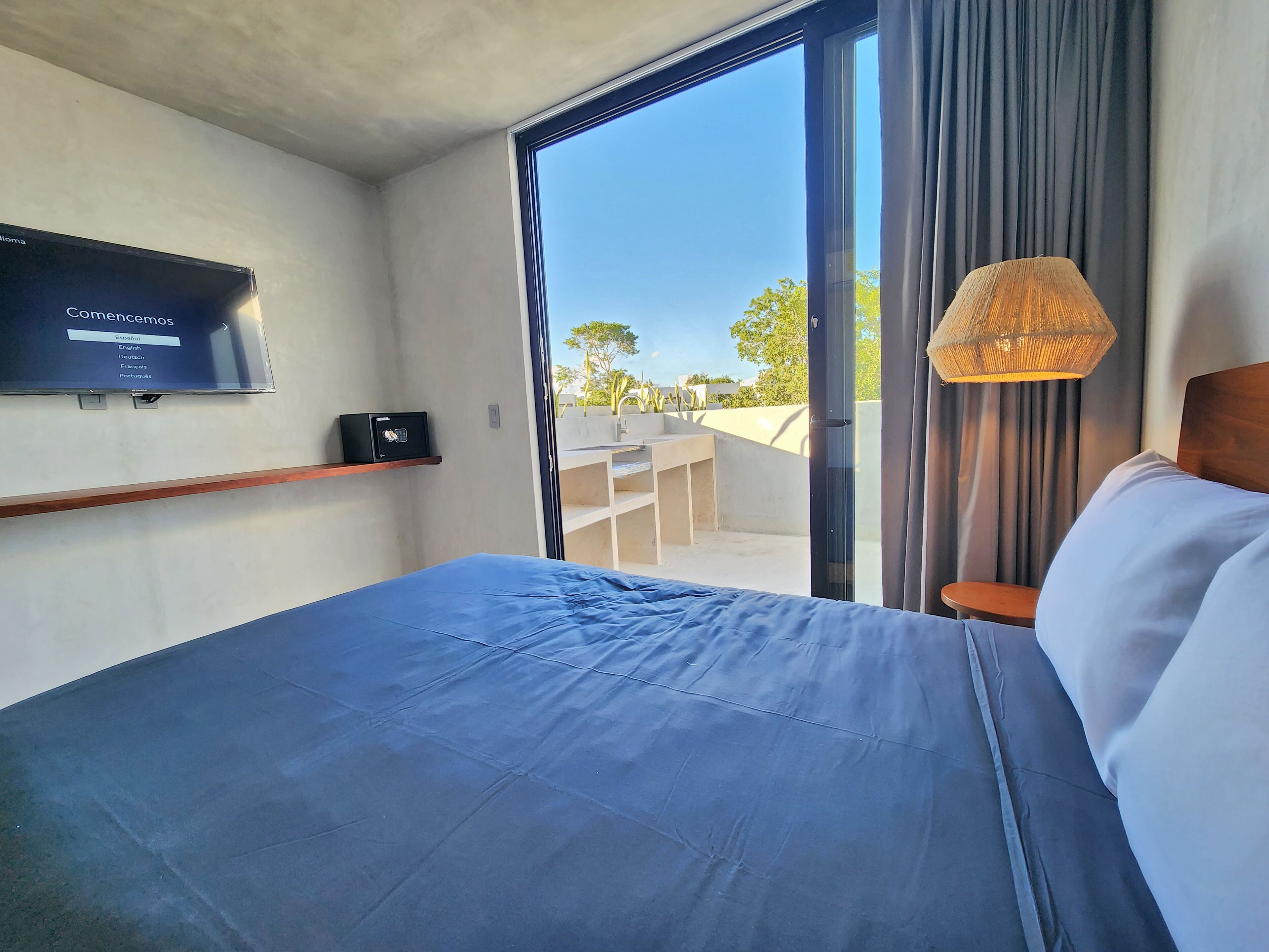 A hotel room with a bed, a television on the wall, a safe, and a view of the outside.