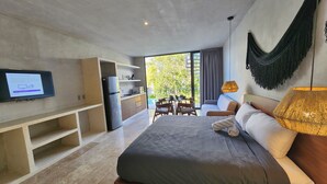 Ett modernt hotellrum med en stor säng, en TV som är monterad på väggen, ett litet kök och en balkong med utemöbler.
