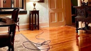 Ein Zimmer mit Holzboden, einem Esstisch mit Stühlen, einer Lampe, einem Spiegel und einer Tür zu einem anderen Raum.