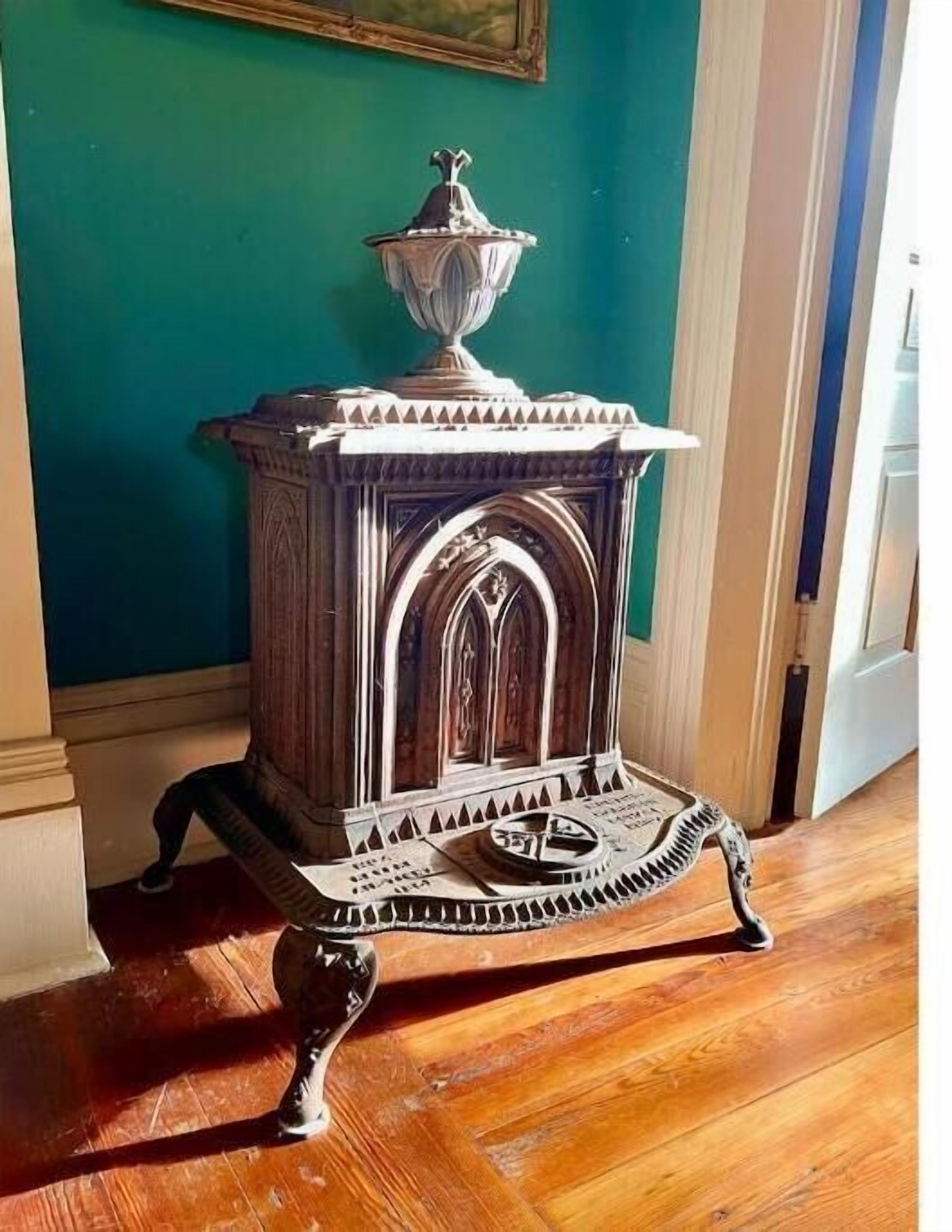 A wooden stove with intricate carvings and a decorative top, placed on a wooden floor against a teal wall.