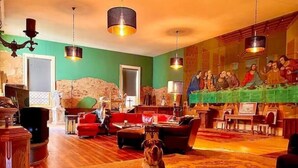 Ein geräumiges Wohnzimmer mit einem großen Gemälde einer biblischen Szene, Holzboden und einem Hund, der auf einem Teppich sitzt.