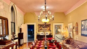 Ein Esszimmer mit einem langen Holztisch, roten Stühlen und einer Chandelier. Ein Sofa und ein Gemälde sind an der Wand zu sehen.