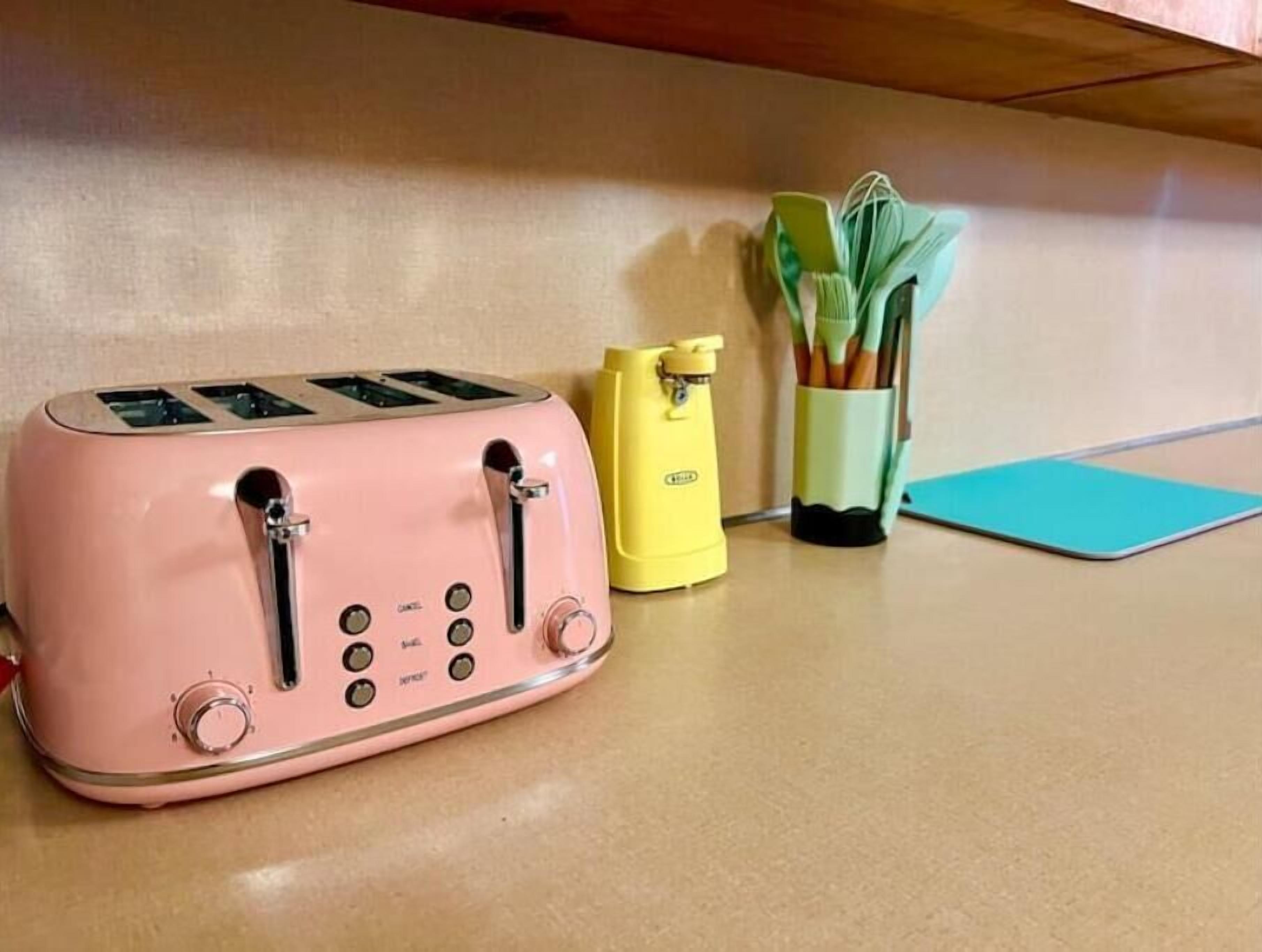 A pink toaster on a kitchen counter with a yellow can opener and a green utensil holder.