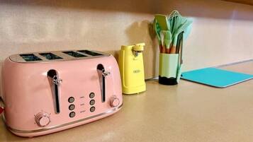 A pink toaster on a kitchen counter with a yellow can opener and a green utensil holder.