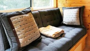 L’intérieur chaleureux d’un chalet en bois, avec un canapé et deux coussins, une fenêtre et un plafond en bois.