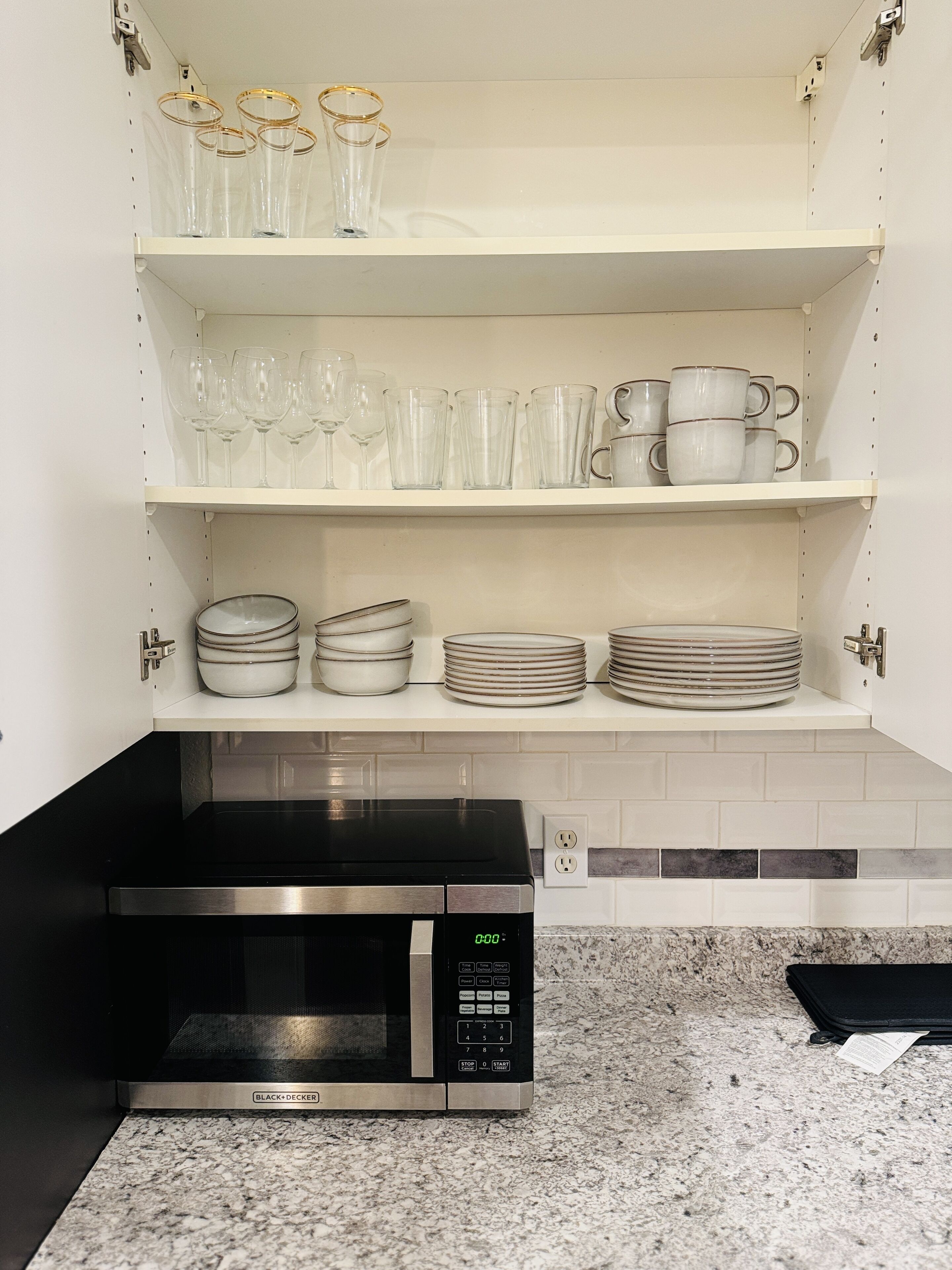 Una cocina con microondas, estantes con cristalería y platos apilados.
