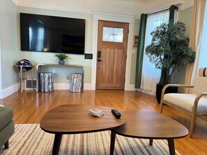 A living room with a flat-screen TV, a wooden door, a potted plant, and a sofa.