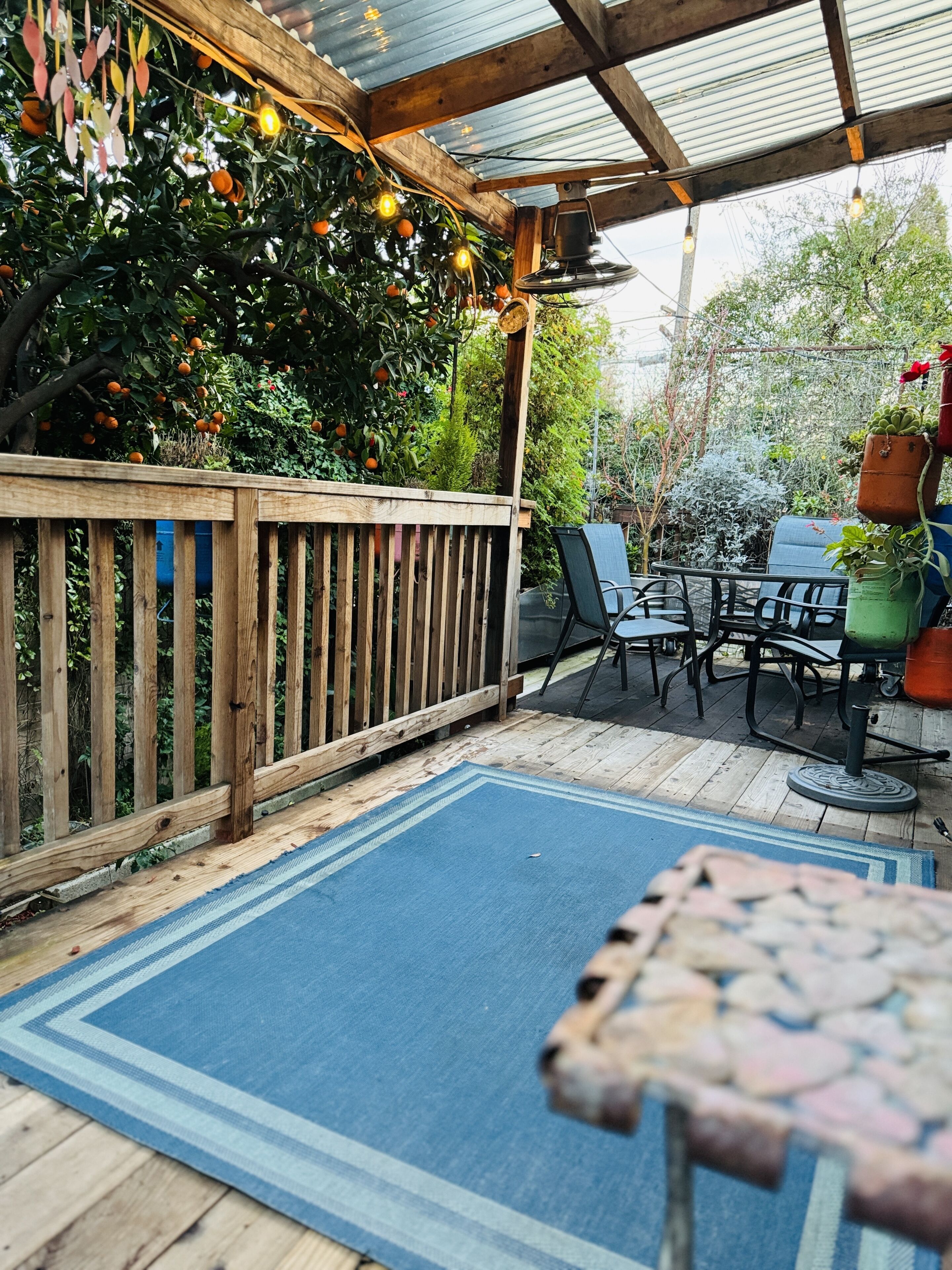A covered patio with a wooden deck, a blue rug, and a table with chairs.