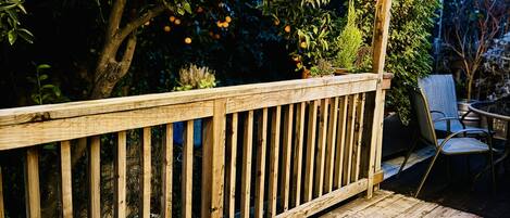 Una terraza de madera con barandilla, luces colgantes y una pérgola.