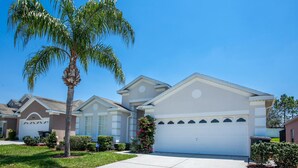 A residential house with a white garage, a palm tree, and a well-maintained lawn. - Free Pool Heat & Spacious Pool Deck | Themed Bedrooms | Near Disney (Kissimmee)