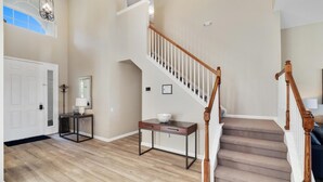 A spacious foyer with a wooden staircase, a coat rack, a console table, and a door. - Spacious 5 Bedroom Villa w/ Themed Bedrooms, Theater Room, and Free Pool Heat (Kissimmee)