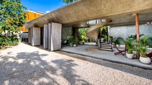 A modern building with a concrete facade, outdoor seating area, and potted plants. - Seremonia Origen by The Spot Rentals (Tulum)