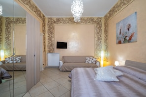 Une chambre d’hôtel dotée d’une armoire à portes miroir, d’un téléviseur à écran plat, d’un canapé, d’un lit et d’un tableau au mur.