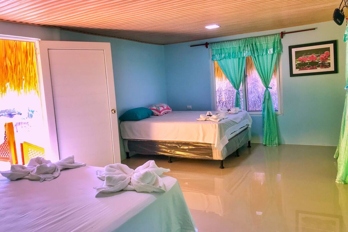 A bedroom with a bed, a window with curtains, a door, and a framed picture on the wall.