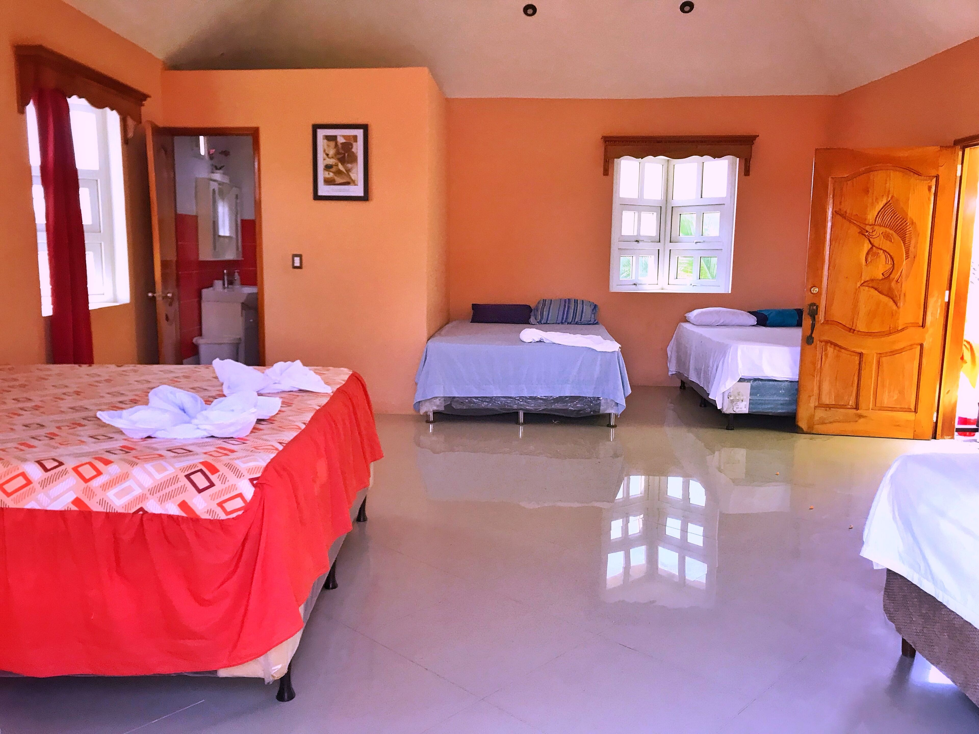 Habitación de hotel con dos camas, una puerta de madera, una ventana con contraventanas blancas y un cuadro enmarcado en la pared.