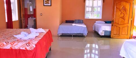 Habitación de hotel con dos camas, una puerta de madera, una ventana con contraventanas blancas y un cuadro enmarcado en la pared.