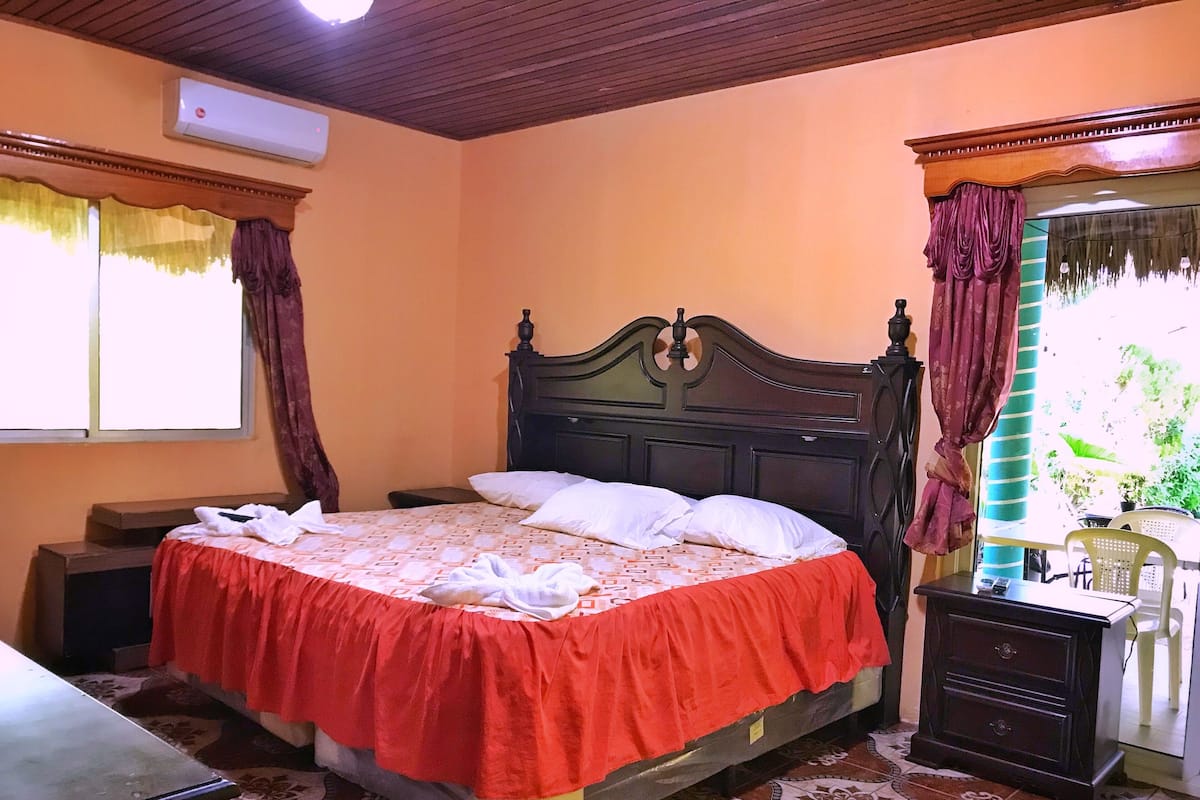 A bedroom with a bed, a nightstand, a dresser, and a window with curtains.