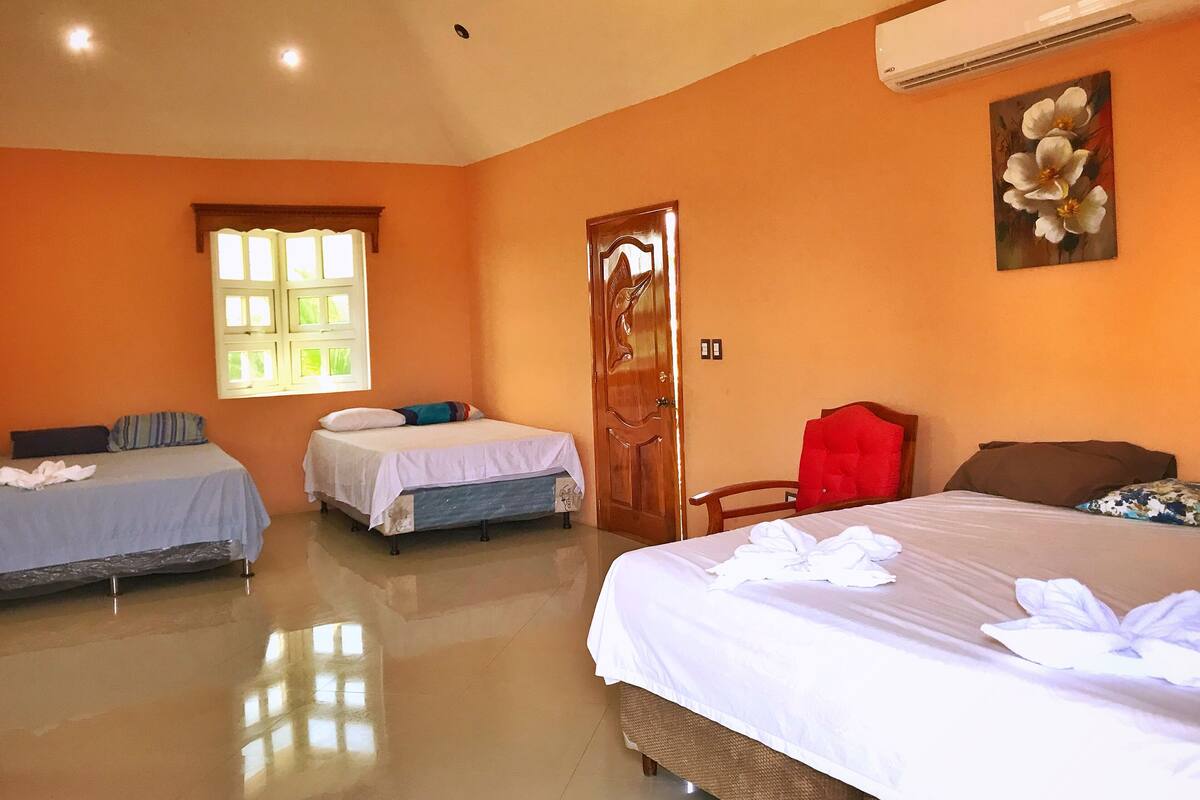 A hotel room with three beds, a large window, and an air conditioning unit.