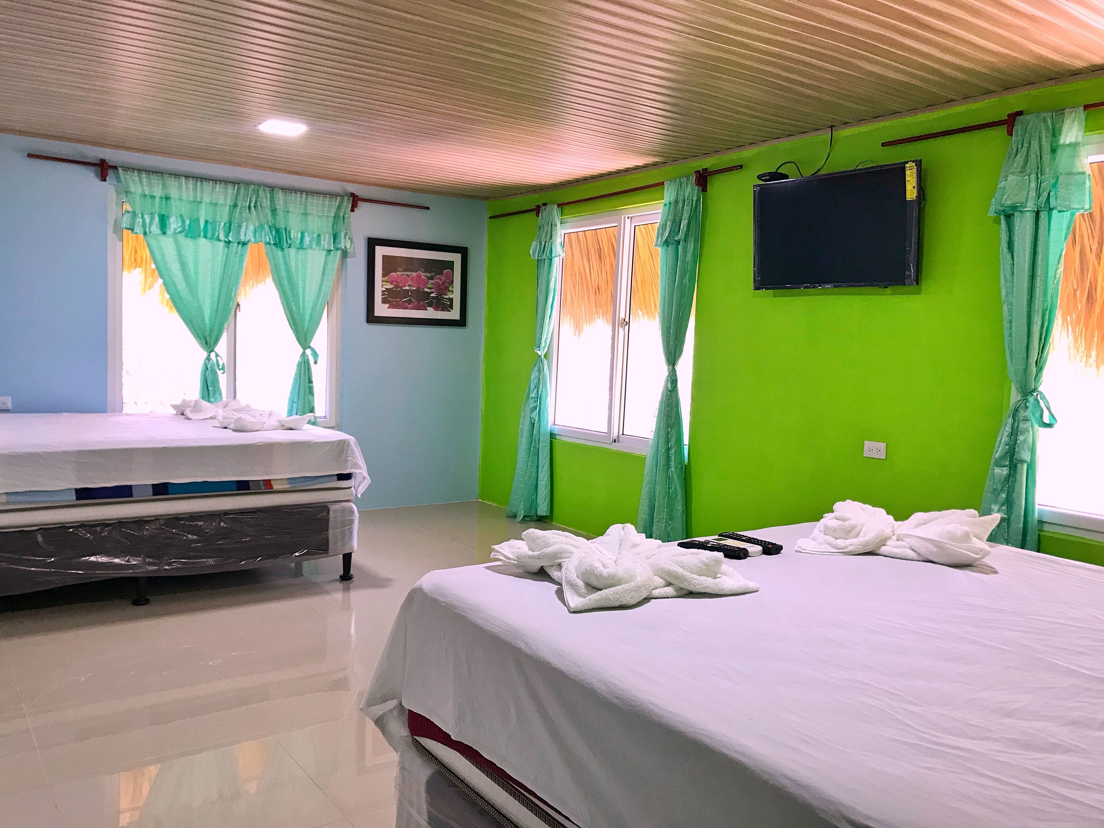 A hotel room with a bed, a small bedside table, a TV mounted on the wall, and a window with curtains.