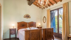 Une chambre à coucher avec un lit en bois, des lampes de chevet, un lustre, une fenêtre avec des rideaux et une vue sur la verdure à l’extérieur.