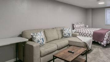 A modern, compact living space with a sectional sofa, a small coffee table, and a bed with patterned bedding.
