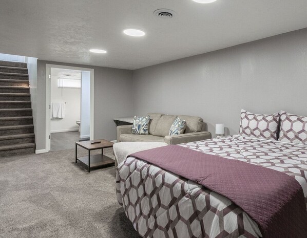 Ein Schlafzimmer mit einem Bett, einem Sofa, einem kleinen Tisch und einer Treppe, die in einen anderen Raum führt.